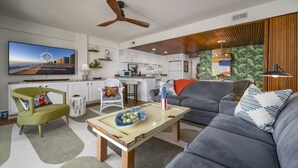 Una sala de estar moderna con un sofá gris, un sillón verde, una mesa de centro de madera y un televisor montado en la pared.