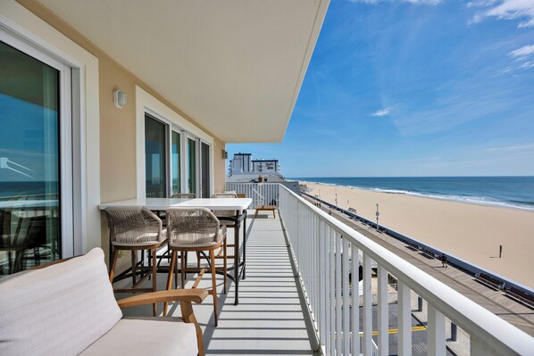 A balcony with a view of the beach, furnished with a sofa, chairs, and a table.