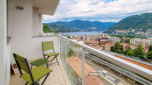 Een balkon met twee stoelen en een tafeltje, met uitzicht op een stadslandschap met bergen en een wateroppervlak.