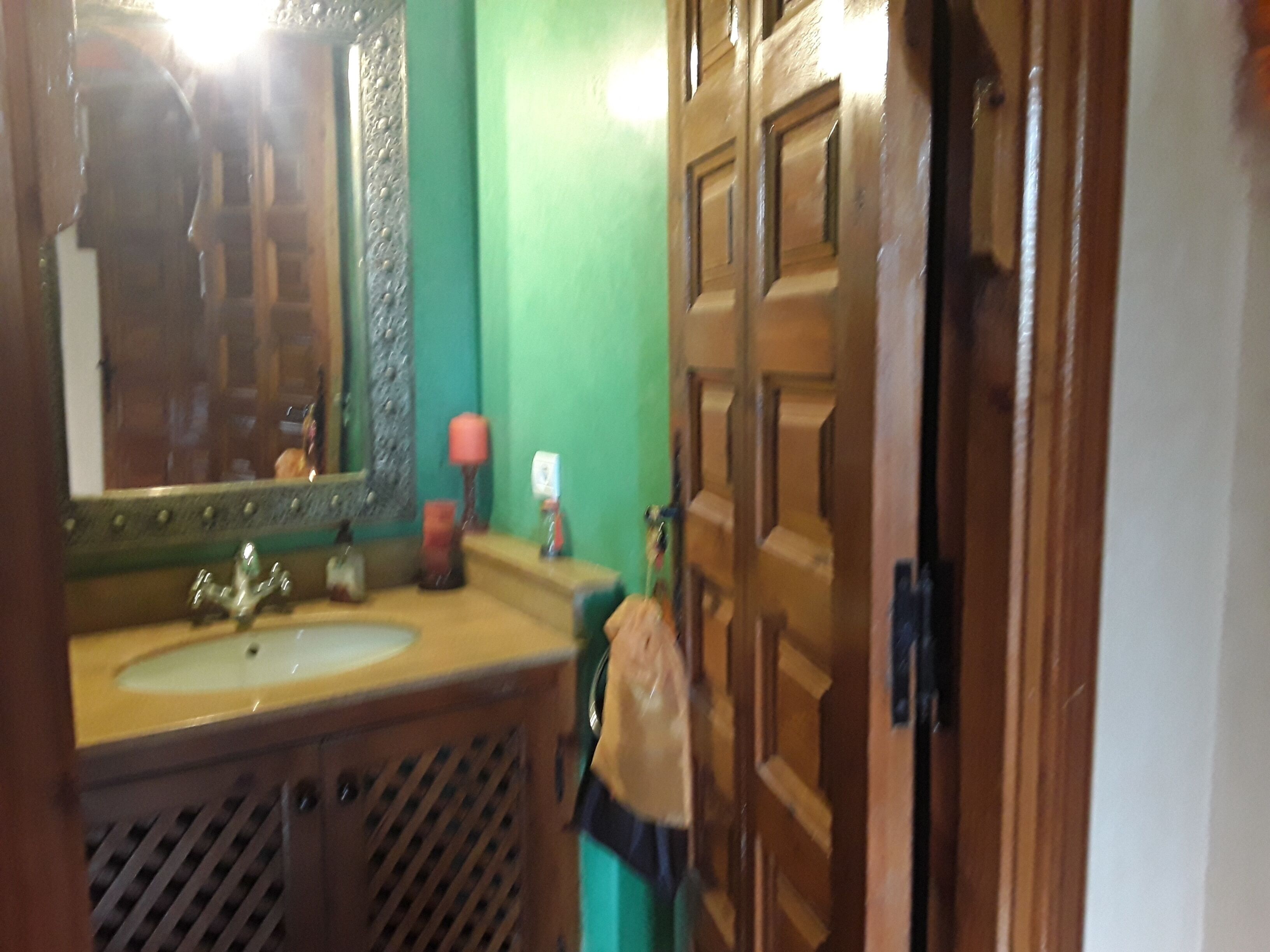 A bathroom with a wooden door, a green wall, and a sink with a mirror.