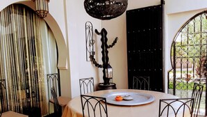 Een eetgedeelte met een ronde tafel, stoelen, een decoratief kunstwerk aan de muur en uitzicht door een open deur.