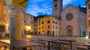 A historic square with a prominent church featuring a clock tower and a rose window, surrounded by traditional buildings and outdoor seating areas. - Nest In Como - A Nest In The City Of Como for 6 (Como)