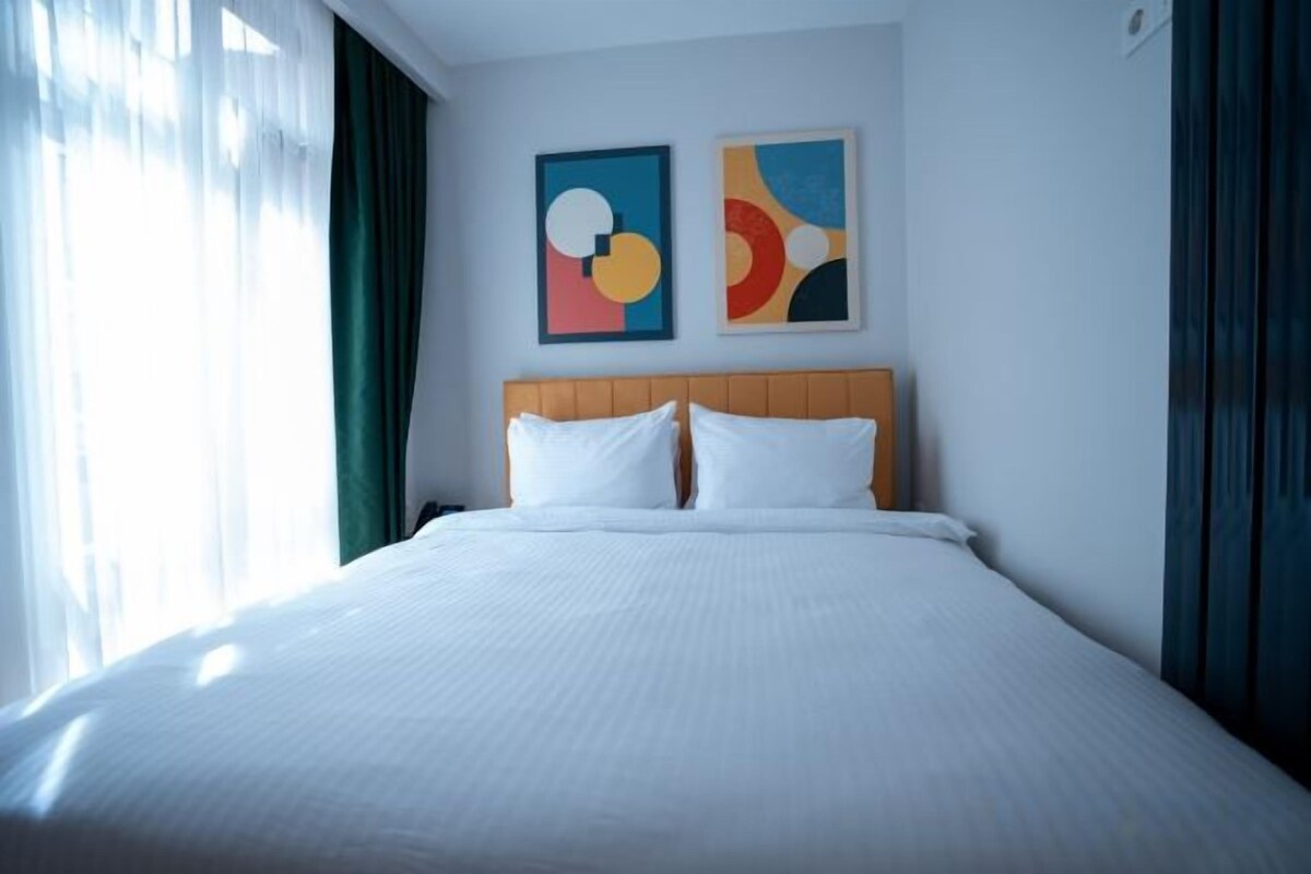 Une chambre d’hôtel avec un grand lit, une tête de lit en bois, deux oreillers blancs et deux tableaux abstraits accrochés au mur.