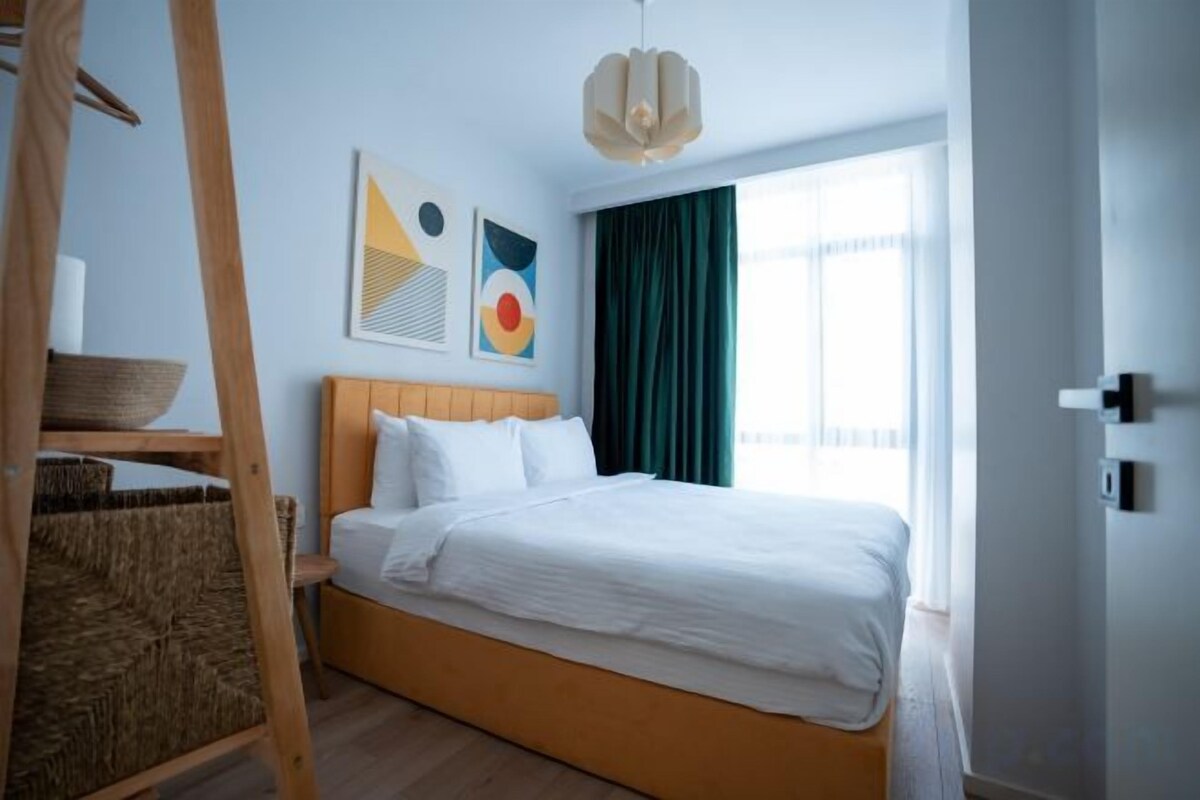 Un lit avec du linge de lit blanc, une tête de lit en bois et un panier posé sur une étagère.
