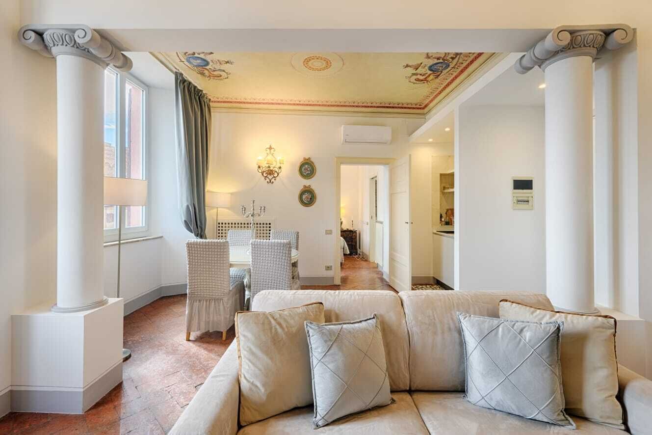A spacious living area with a beige sofa, a dining table with chairs, and a chandelier.