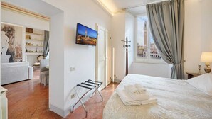 Ein Hotelzimmer mit Bett, Fernseher, Fenster mit Vorhängen, einem Wäscheständer und Blick auf einen Turm.
