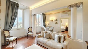 Ein geräumiges Wohnzimmer mit großem Fenster, einer Couch, einem Sessel und einem Essbereich.