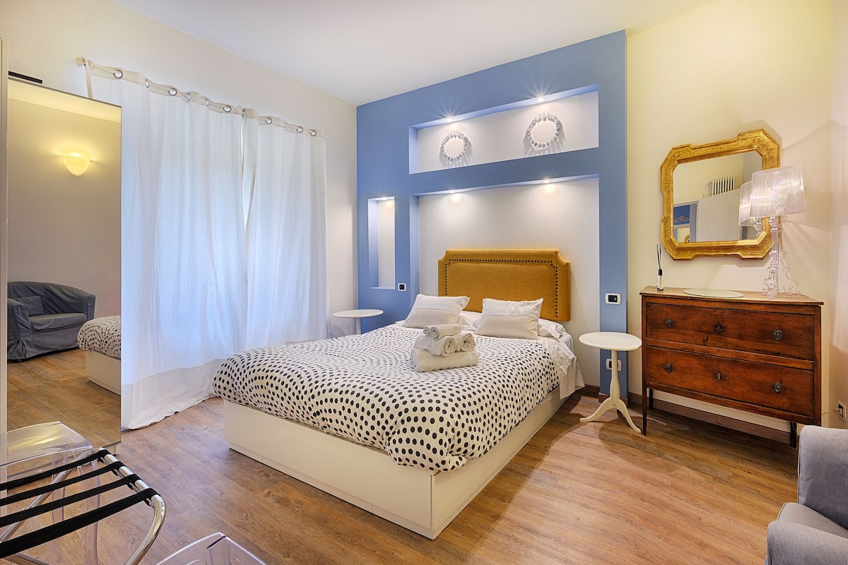 A bedroom with a bed, a dresser, a mirror, and a small table.