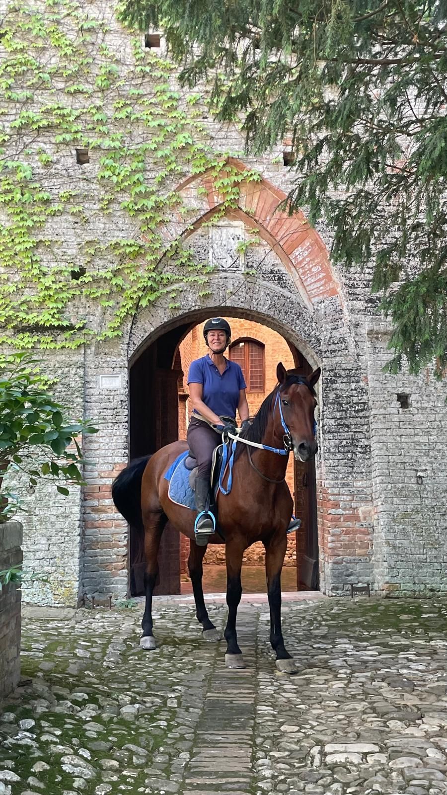A person riding a horse through an arched stone doorway.