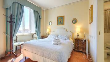 A neatly made bed with a white bedspread, a wooden nightstand with a lamp, and a chair.