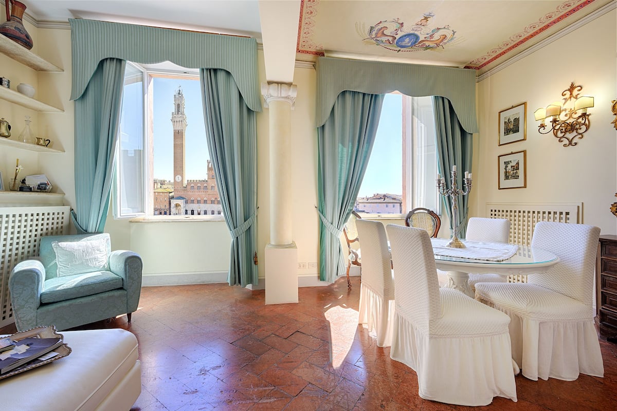 A room with a view of a tower, a dining table with chairs, and a sofa.