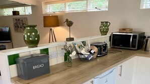 A compact kitchen with a wooden countertop, a bread storage box, a microwave, and a small refrigerator. - Little Innsacre (Shipton Gorge)