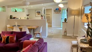 A modern living room with a purple sofa, a dining area with a white table, and a kitchen in the background. - Little Innsacre (Shipton Gorge)