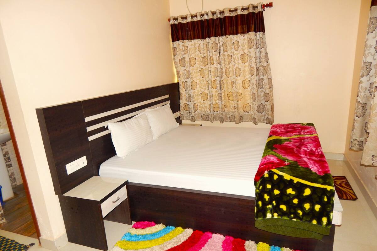 Une chambre à coucher avec un lit, une table de chevet, un tapis coloré et une fenêtre avec des rideaux.