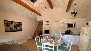 A cozy room with a bed, a dining table with chairs, a kitchen area with appliances, and a staircase. - Cozy 2-BR House with Terrace, Near Forest and Beaches, Sleeps 6 (Saint-Jean-de-Monts)
