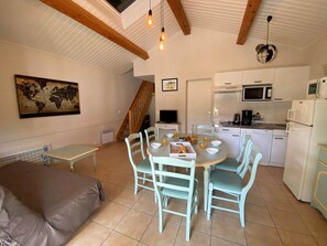 Una habitación acogedora con una cama, una mesa de comedor con sillas, una zona de cocina con electrodomésticos y una escalera.
