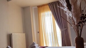 A hotel room with a neatly made bed, a radiator, and a window with curtains. - HOTEL AKROPOL (Katerini)