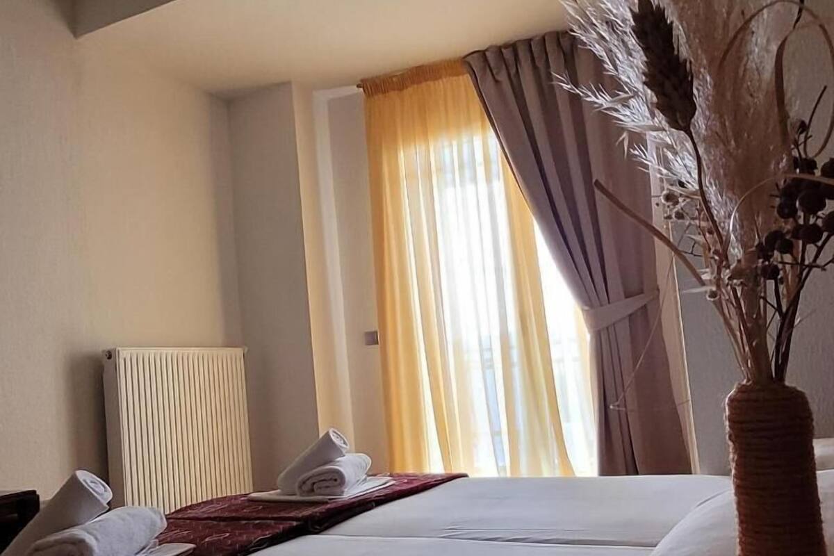 A hotel room with a neatly made bed, a radiator, and a window with curtains.