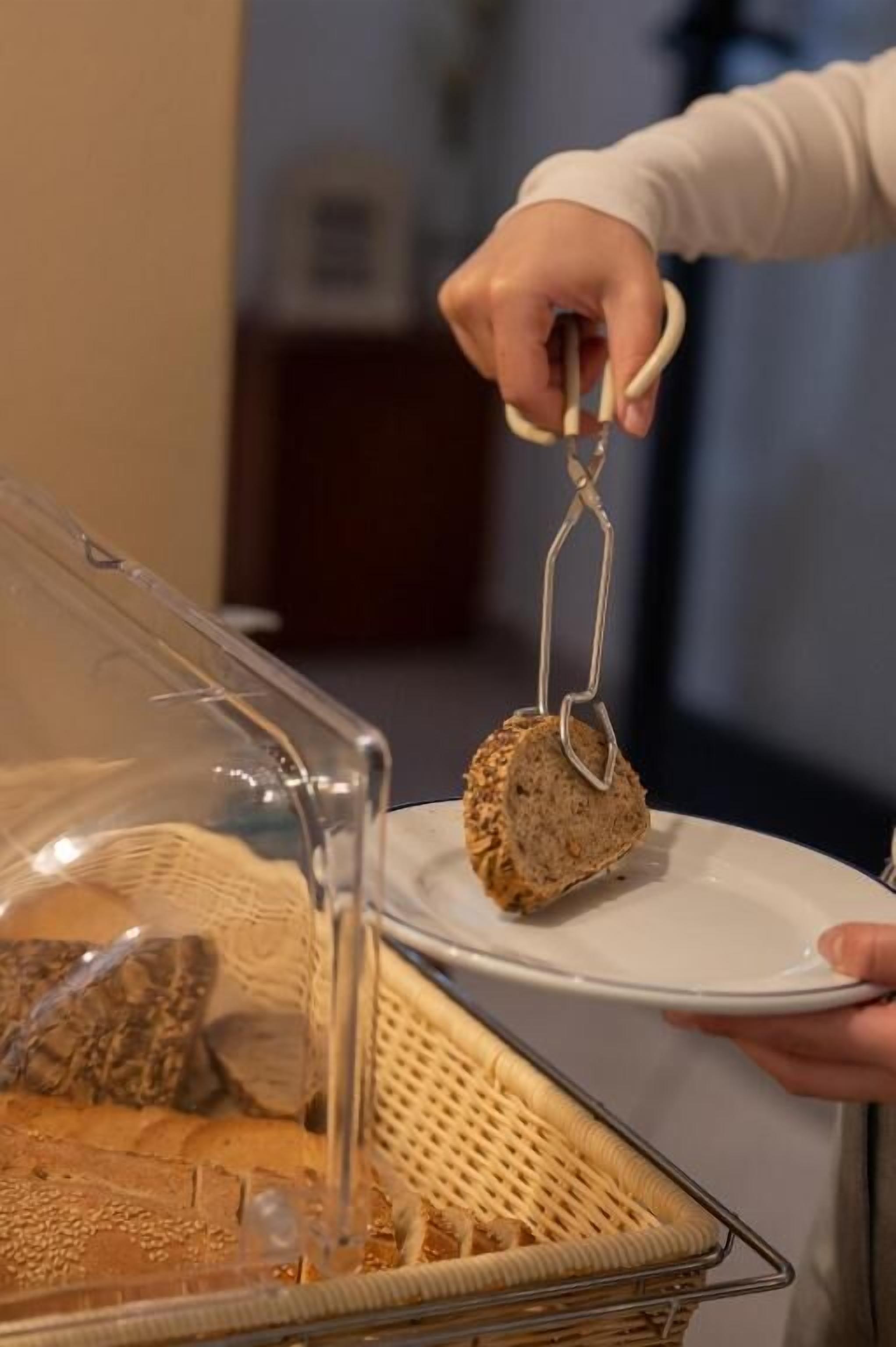 Una mano usando unas pinzas para servir comida de un recipiente transparente.