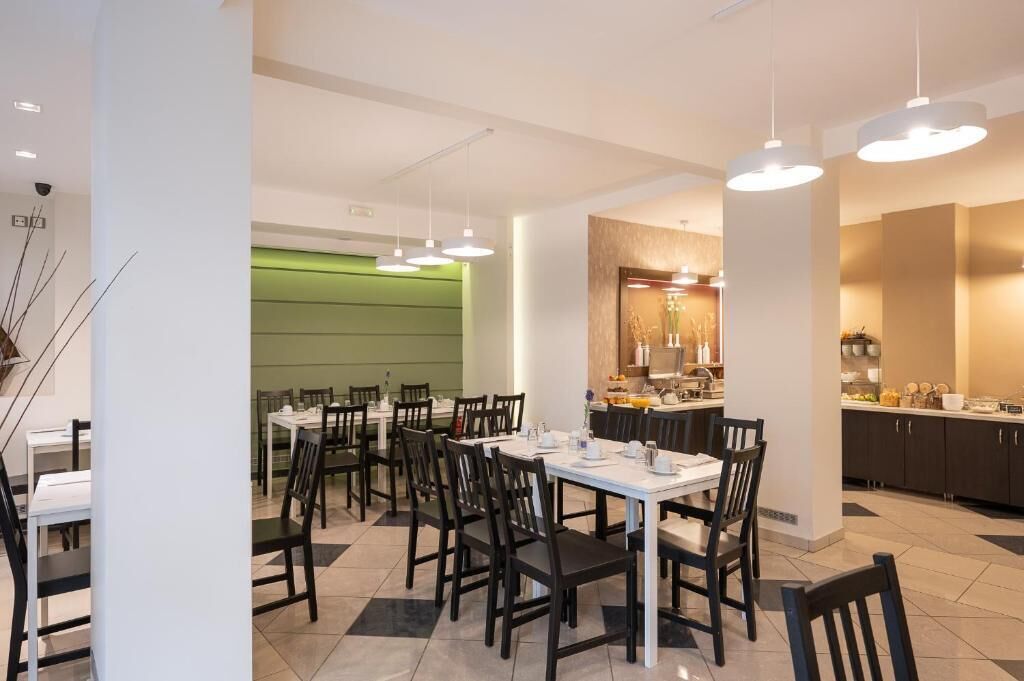 Un comedor moderno con mesas y sillas, una cocina al fondo e iluminación colgante.