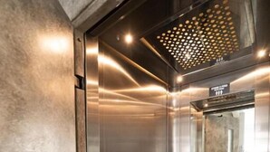 A modern elevator with metallic walls and a reflective floor, featuring a control panel and a light fixture. - HOTEL AKROPOL (Katerini)