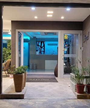 A modern hotel entrance with a welcoming mat, potted plants, and a view into the interior. - HOTEL AKROPOL (Katerini)