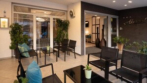 A modern indoor seating area with glass doors leading to a balcony, furnished with black chairs and tables, and decorated with potted plants. - HOTEL AKROPOL (Katerini)