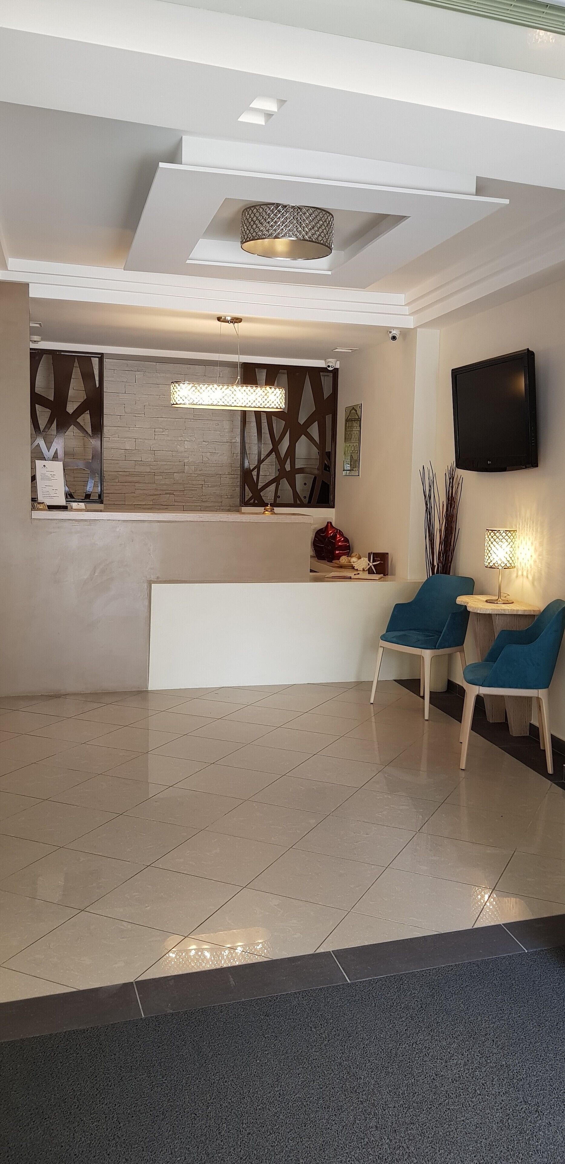 A modern reception area with a reception desk, two blue chairs, a flat-screen TV, and decorative wall panels.
