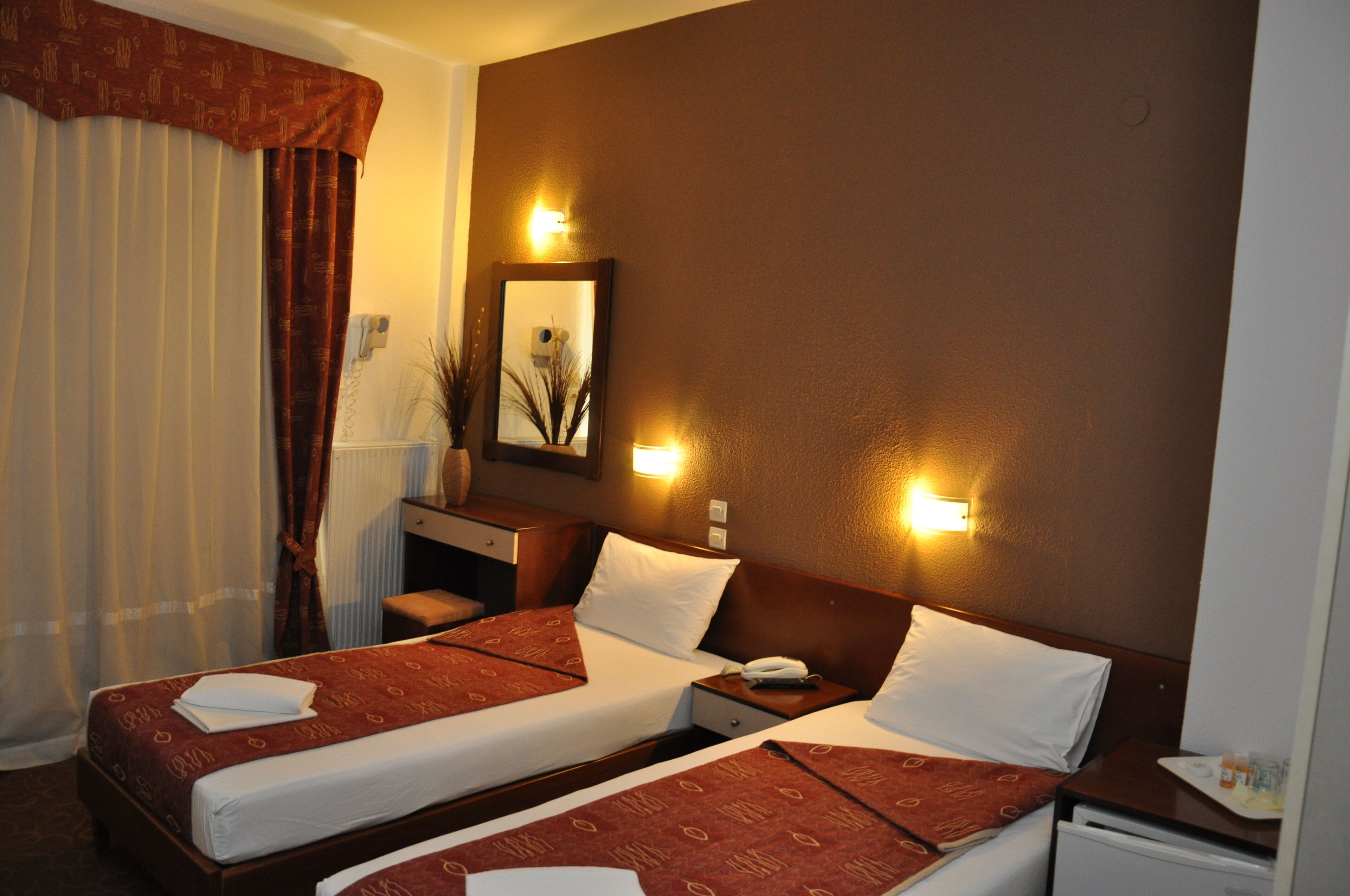 A hotel room with two beds, a desk, a mirror, and a nightstand.
