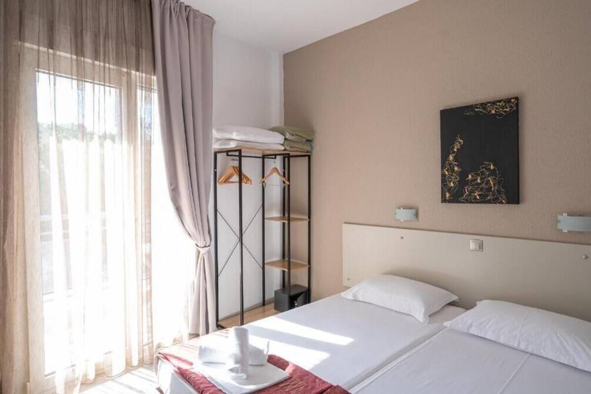 A hotel room with a bed, a wardrobe, a painting on the wall, and a window with curtains.