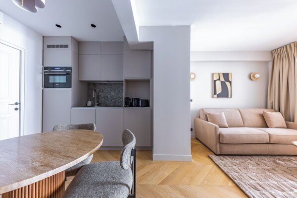 A modern kitchen with built-in appliances, a dining area with a wooden table and chairs, and a living area with a sofa and a rug. - Aparthotel Quartier Libre Opéra (Paris)