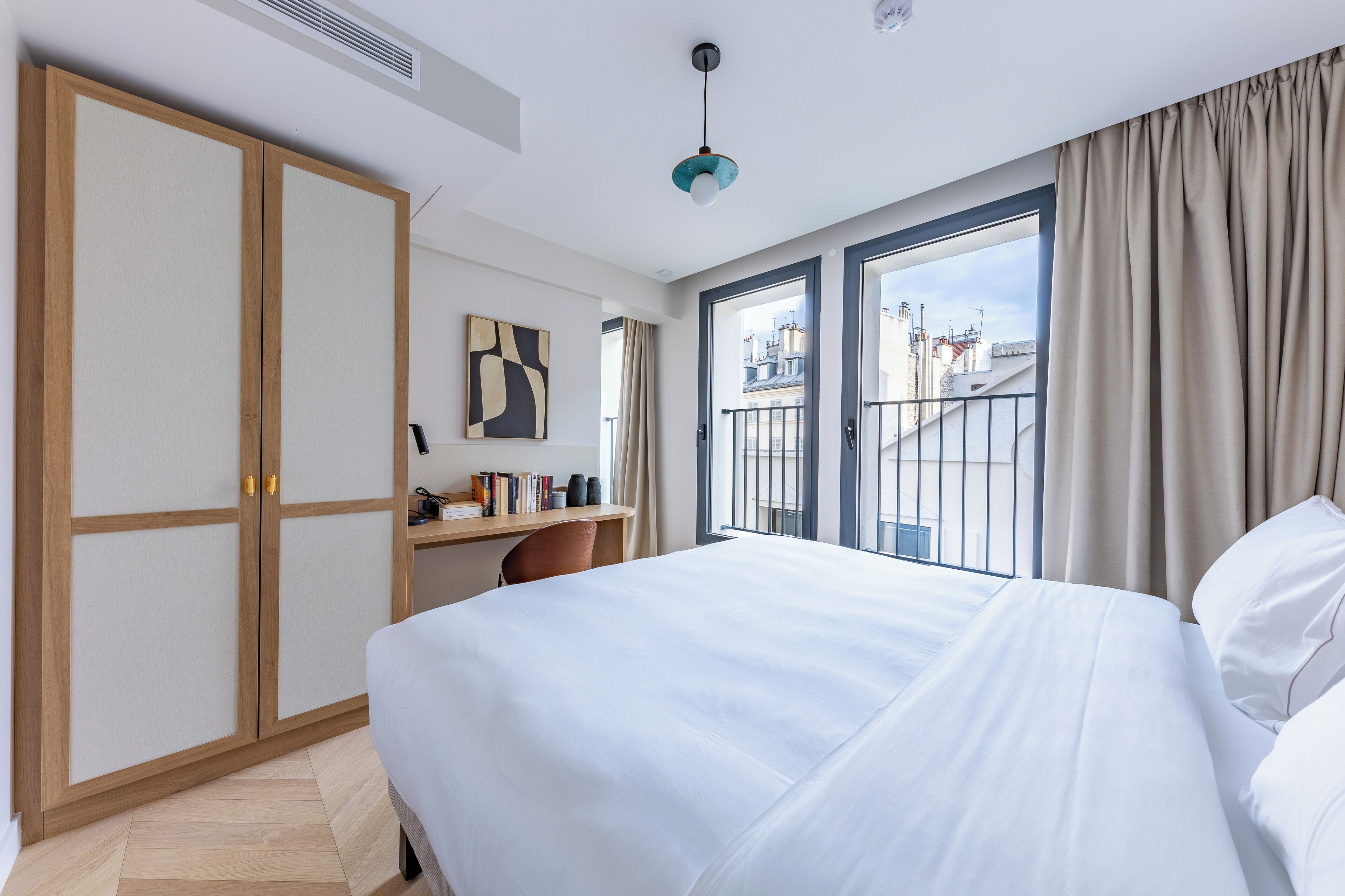 Una habitación de hotel con cama, escritorio, armario y vistas a la ciudad.