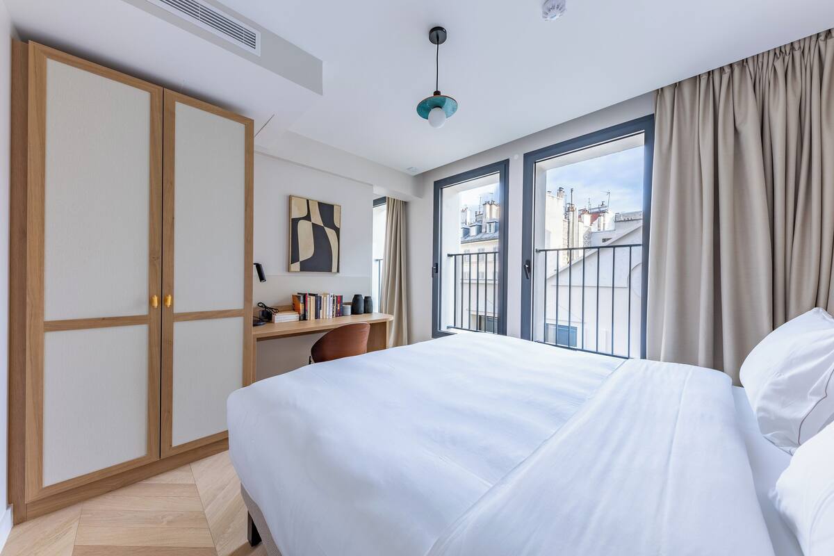 Hotelkamer met een bed, een bureau, een kledingkast en uitzicht op de stad.