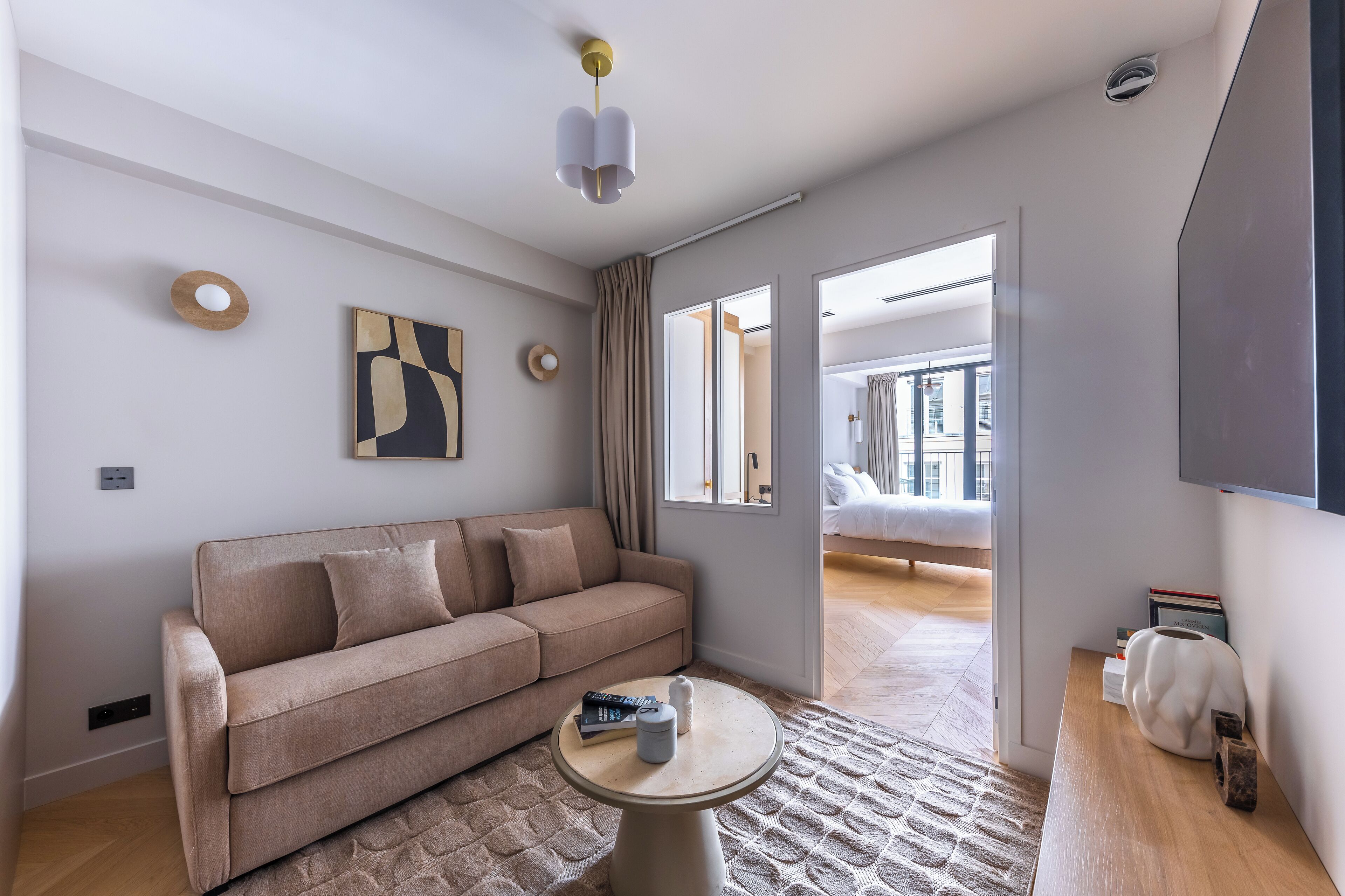 A modern living room with a beige sofa, a round coffee table, and a large window.