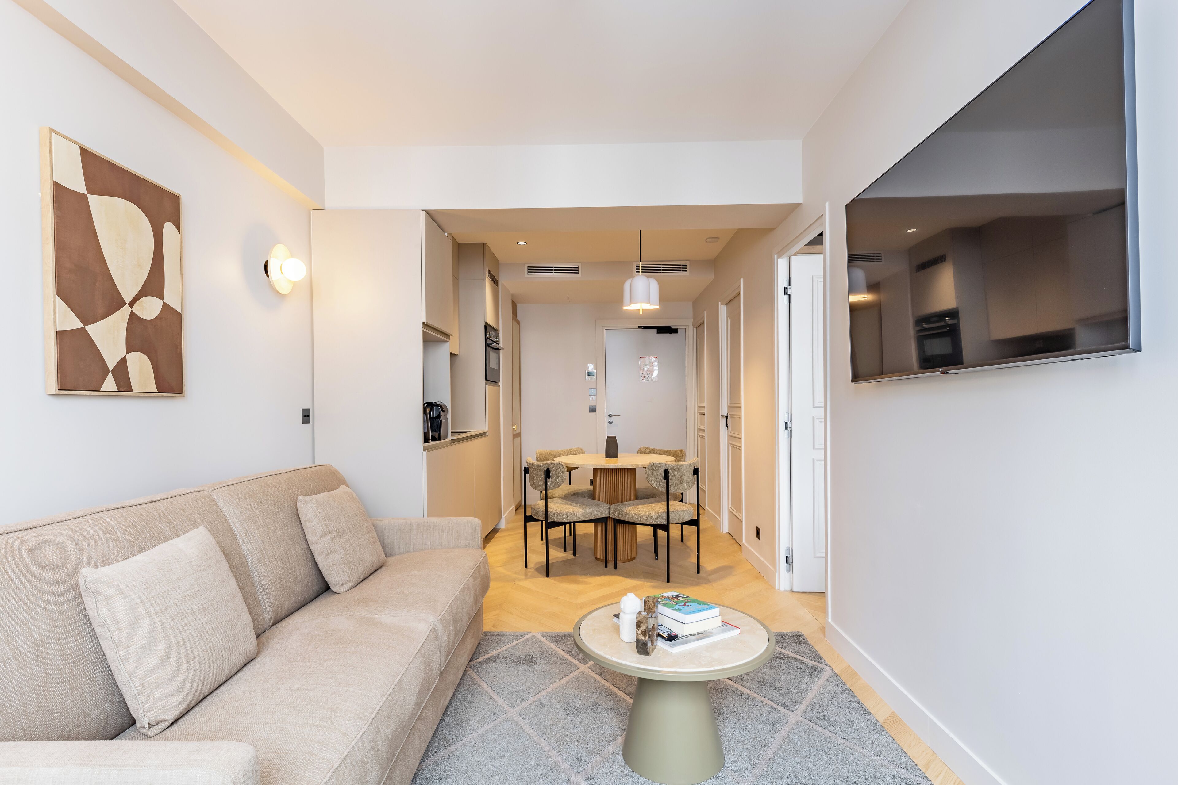 Ein modernes Wohnzimmer mit einem beigen Sofa, einem runden Couchtisch und einem Essbereich mit Tisch und Stühlen.