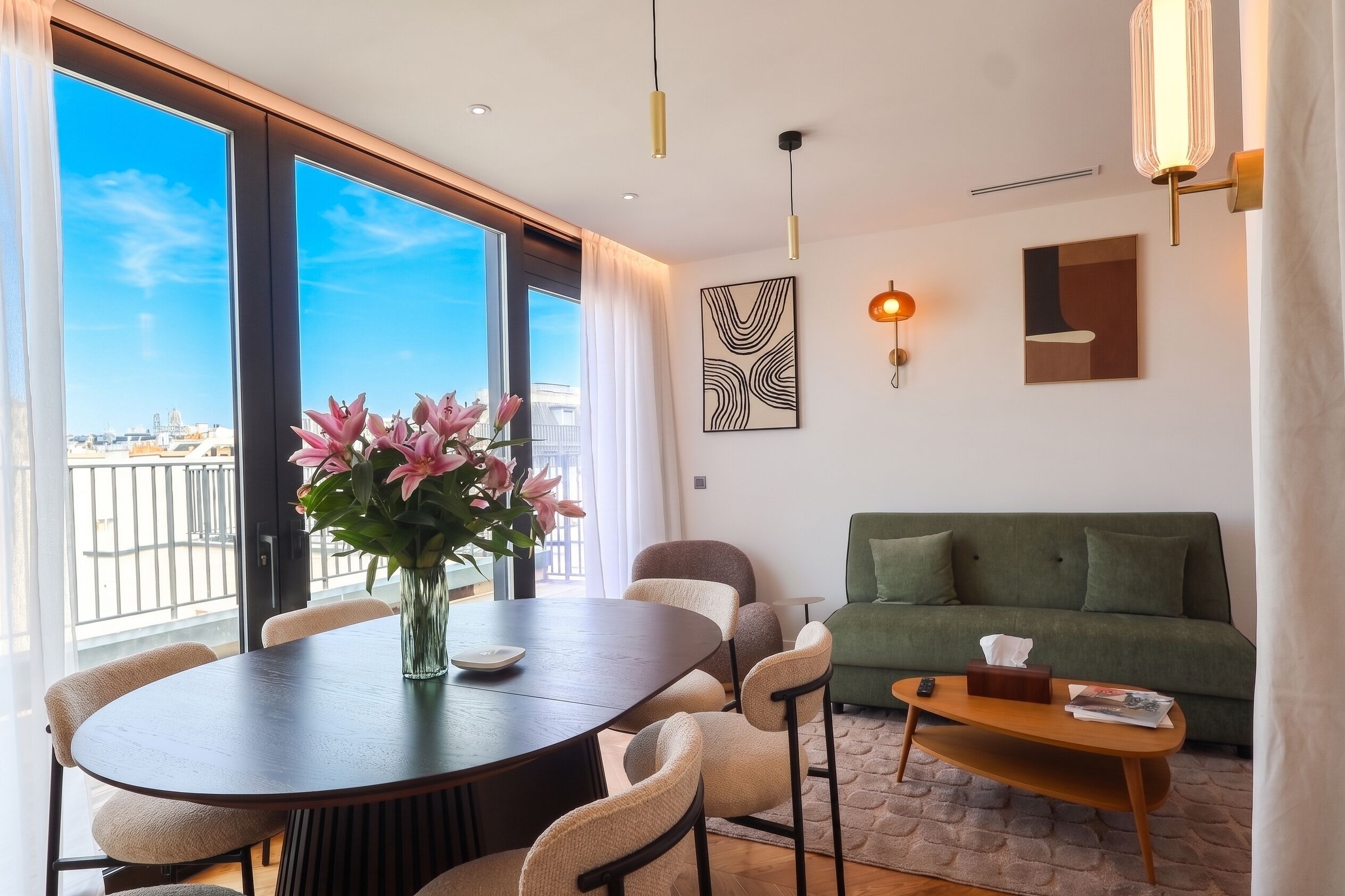 A modern living room with a dining area, a green sofa, and a view of the city through large windows.