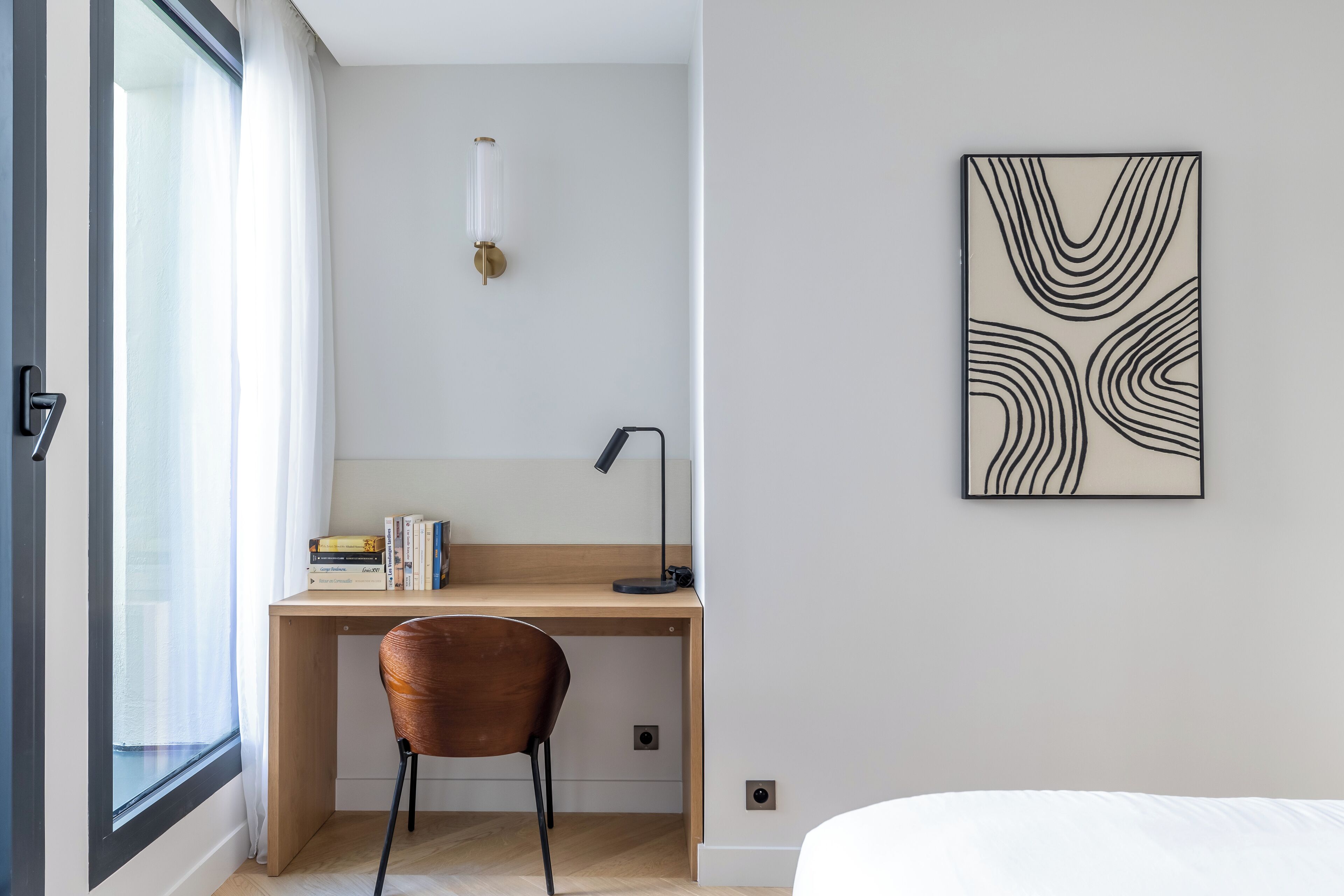 A modern bedroom with a wooden desk, a chair, a bedside table, and a bed.