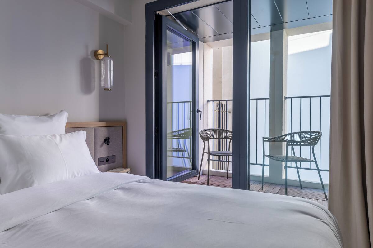 Een hotelkamer met een bed, een nachtkastje, een wandlamp en een balkon met twee stoelen.