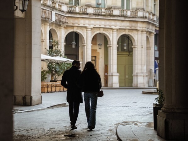 A couple walking in a historic courtyard with classical architecture, including arches and columns. - Aparthotel Quartier Libre Opéra (Paris)