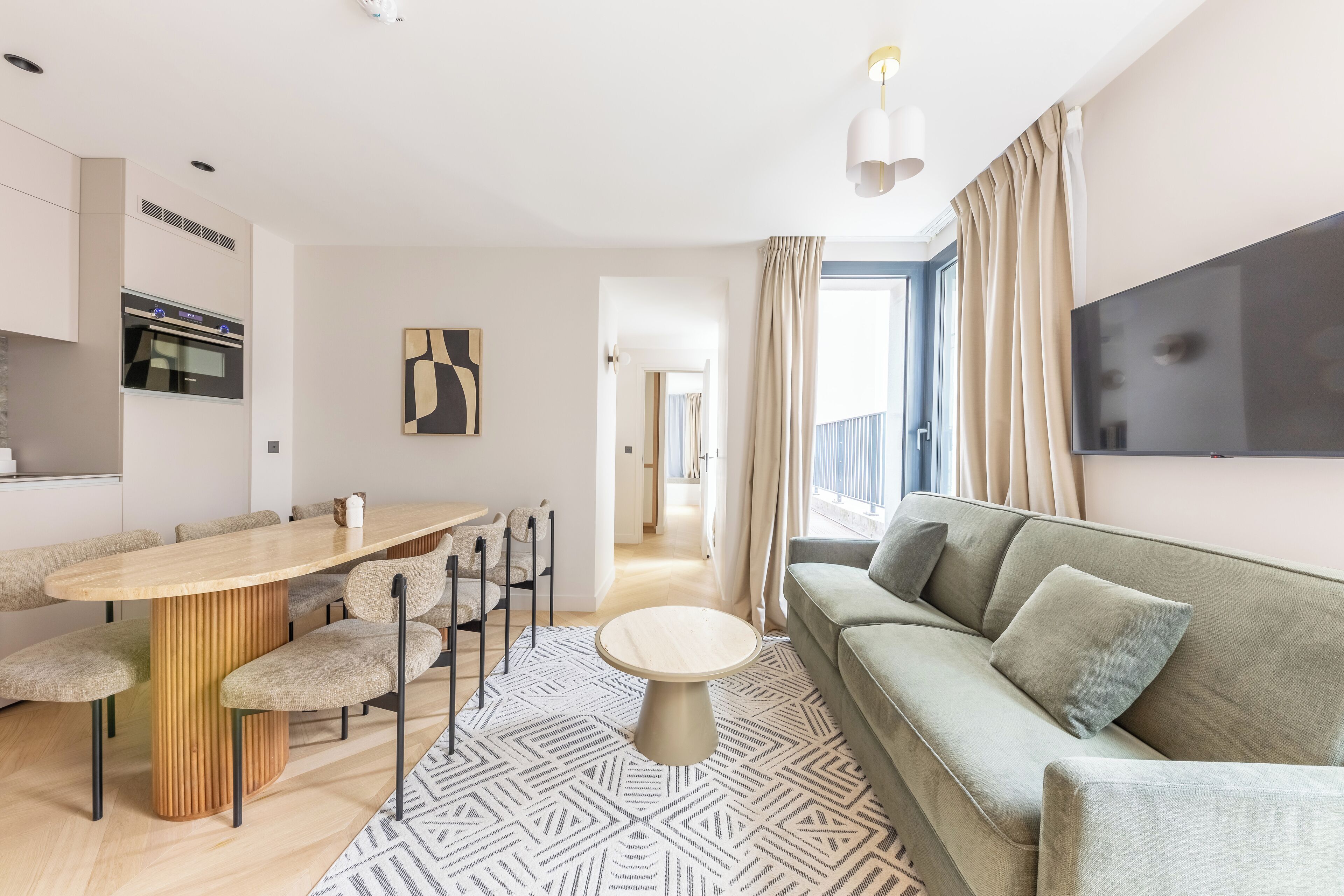 Ein modernes Wohnzimmer mit Essbereich, einer Couch, einem an der Wand befestigten Fernseher und einer Küche mit Backofen.