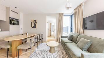 Ein modernes Wohnzimmer mit Essbereich, einer Couch, einem an der Wand befestigten Fernseher und einer Küche mit Backofen.