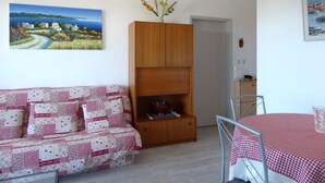 Ein gemütliches Wohnzimmer mit einer Couch, einer Holzkabine, einem Esstisch mit kariertem Tischläufer und einer Pendelleuchte.