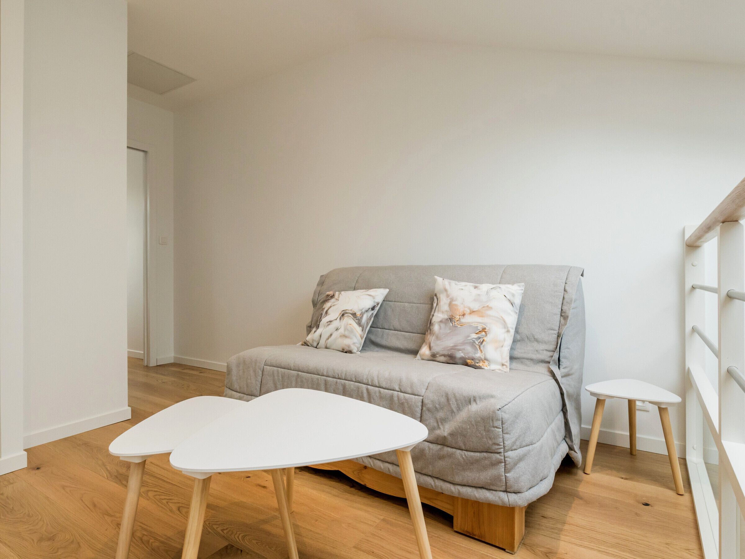Een moderne woonkamer met een grijze bank, twee bijpassende kussens, een witte salontafel en een klein wit krukje.