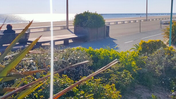 Ein Küstenweg mit Bänken, Straßenlaternen und Blick auf den Strand.