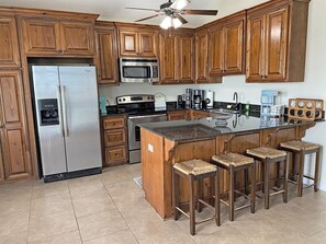 A kitchen with wooden cabinets, a stainless steel refrigerator, a microwave, a stove, and a bar area with stools.