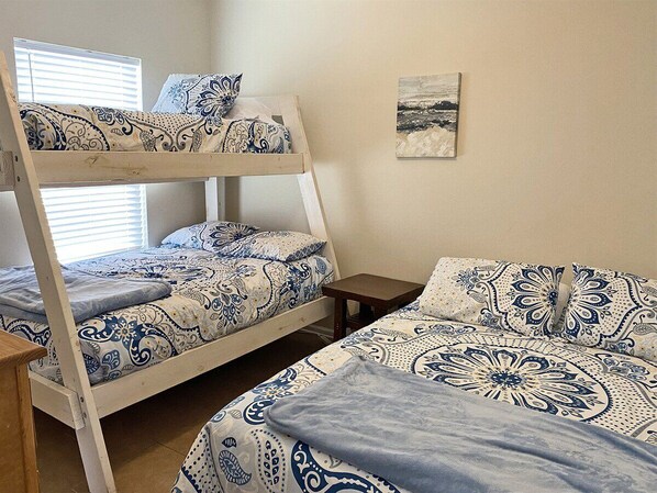 A bunk bed room with patterned bedding, a small bedside table, and a wall-mounted picture.