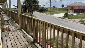 A wooden porch with a railing, a bench, and a palm tree in the background.