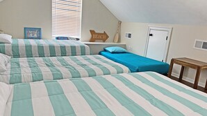 A bedroom with two beds, each with striped bedding, a window with blinds, a door, and a small wooden table.
