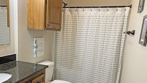A bathroom with a toilet, a shower curtain, wooden cabinets, and a granite countertop.
