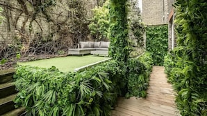 A garden with a wooden deck, a green lawn, and a grey sofa. - Classy 2BR 2BA in the ♥️ of Central London ❄️ Air Con. 🌿 Terrace | Sleeps 6 (Greater London)